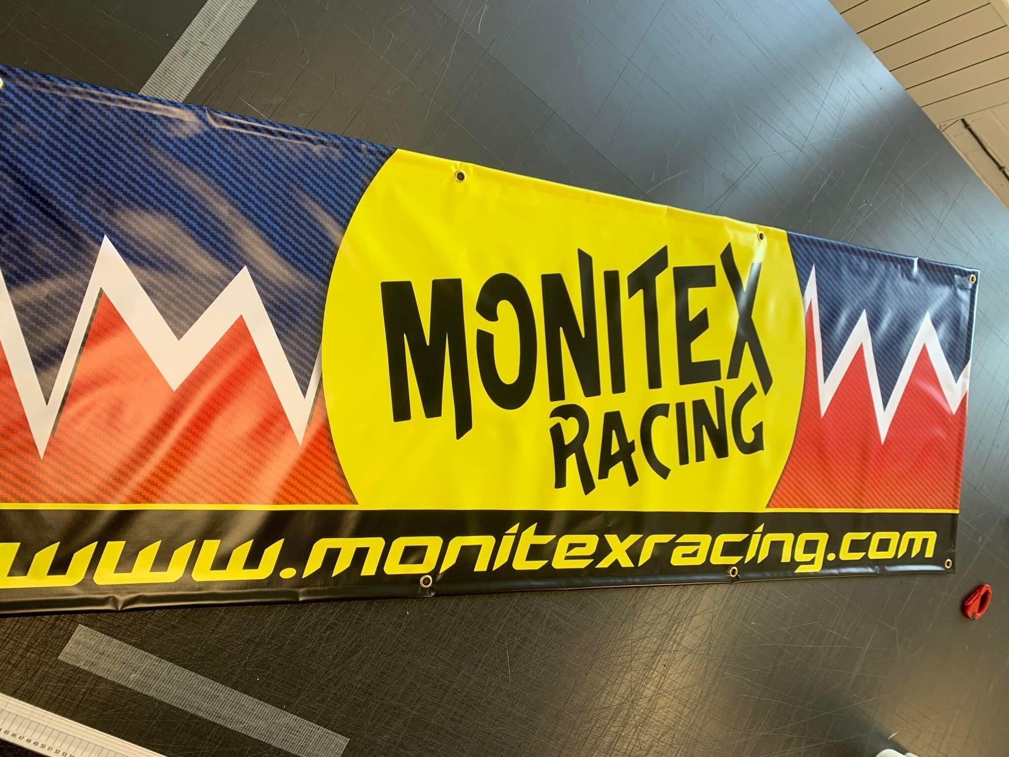 Close-up of a large banner.   The banner is predominantly black, with vibrant yellow, red, and blue sections.   A circular yellow graphic with the words 