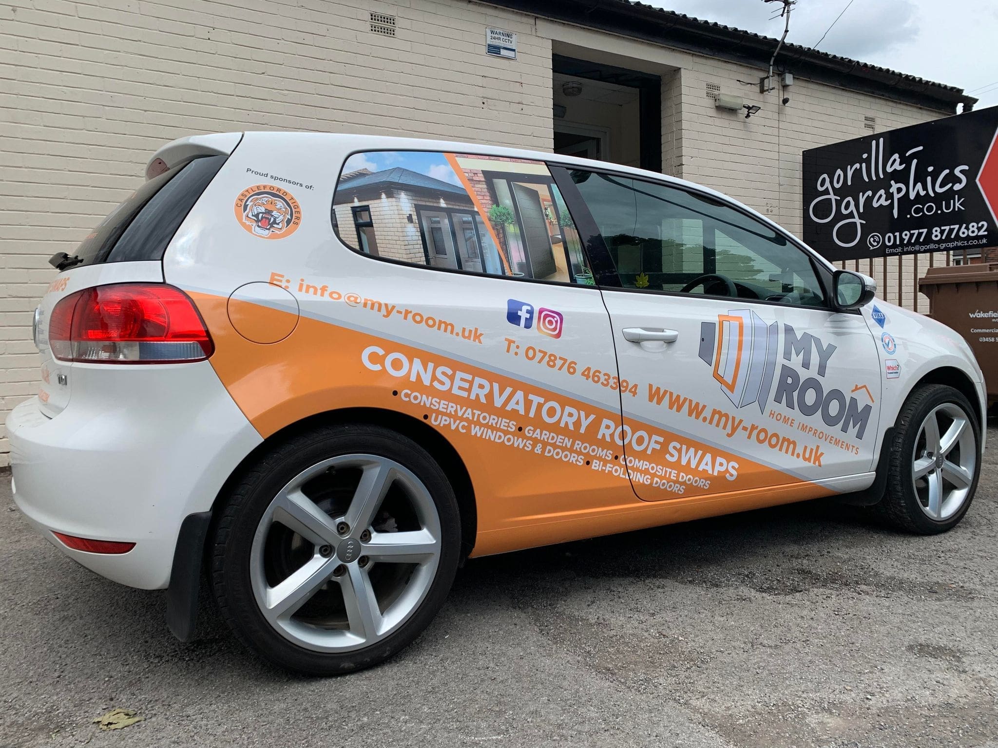 Full outdoor shot of a white car with a large graphic wrap.   The wrap features the company name 